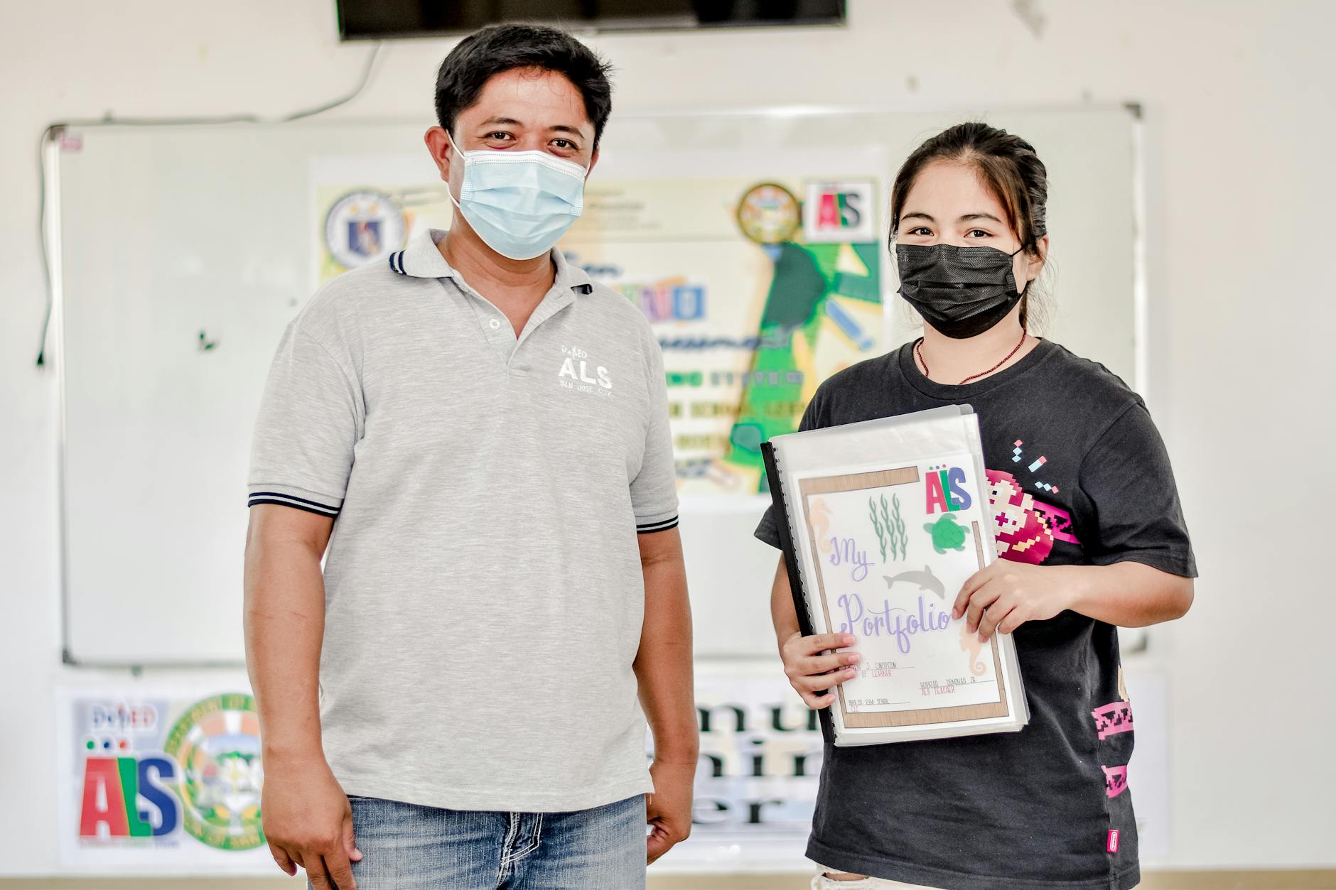 Jak stworzyć portfolio ucznia w edukacji domowej i wykorzystać je przy egzaminach Dwóch azjatyckich uczniów w maseczkach prezentuje materiały edukacyjne