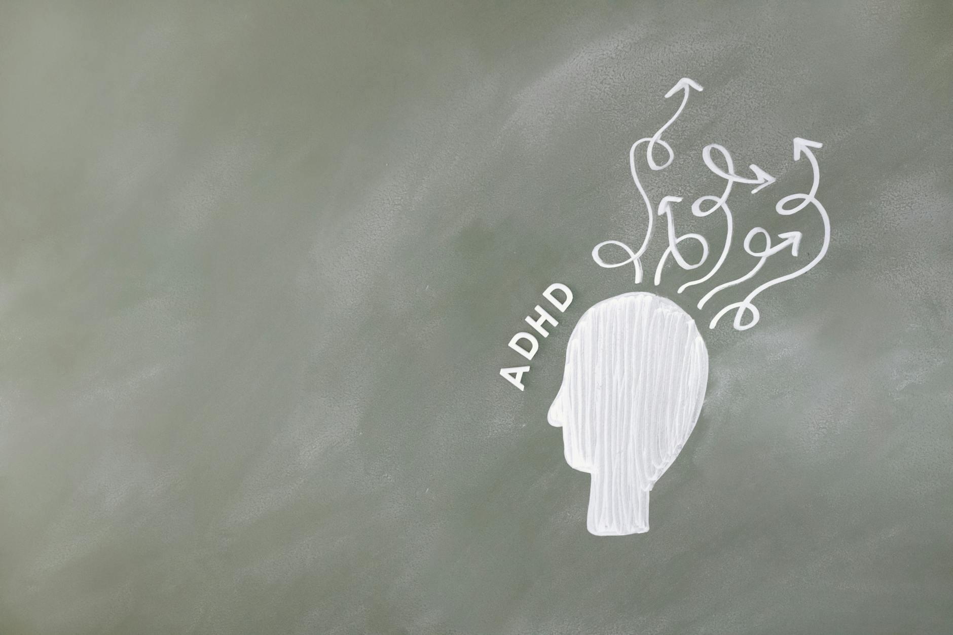 Czy szkoła poradzi sobie z kryzysem uwagi i przebodźcowaniem uczniów? Rysunek głowy z chaotycznymi symbolami ADHD na szkolnej tablicy