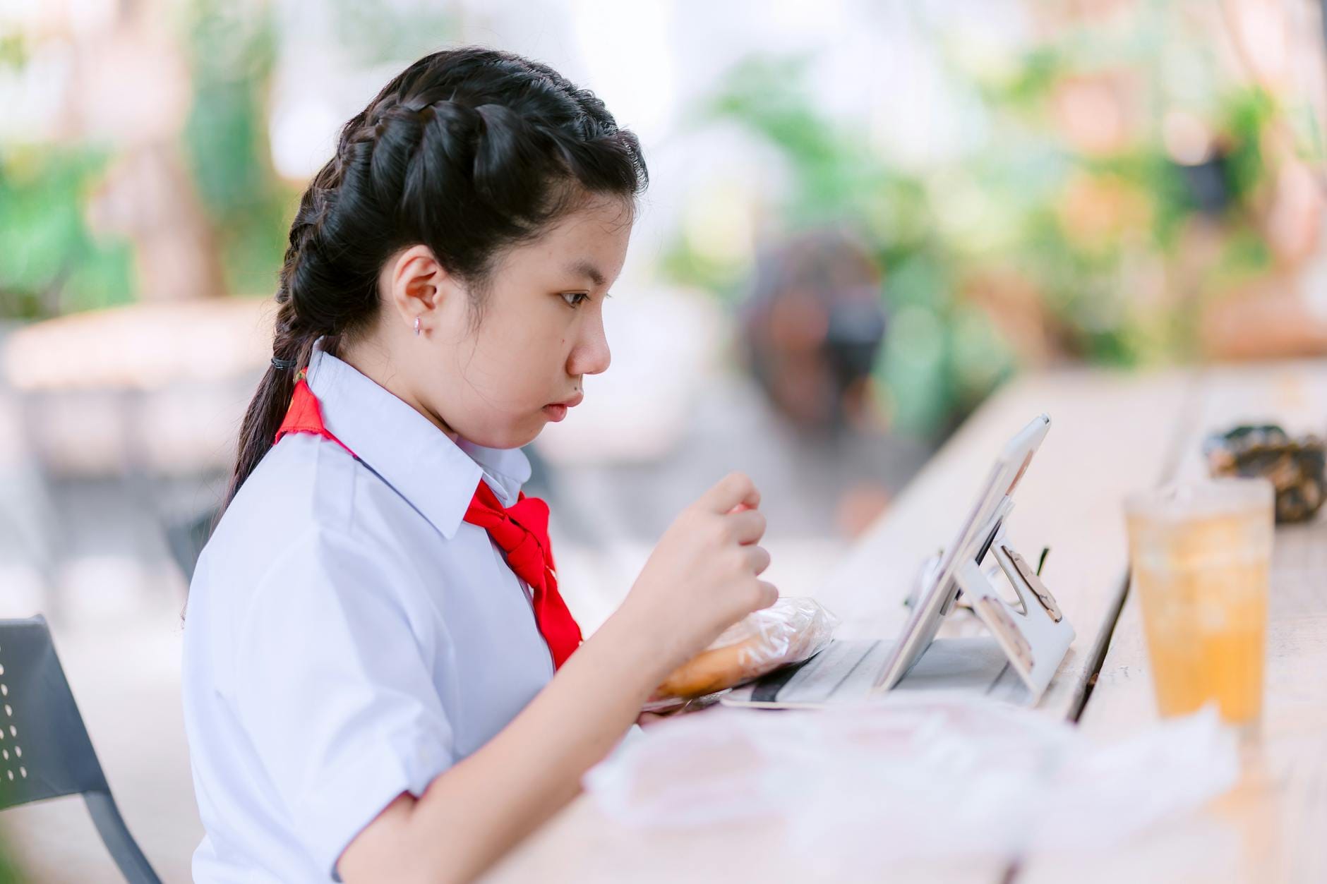 Uczennica w mundurku uczy się na tablecie w kawiarni na zewnątrz