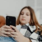 Telefon w szkole a lęk i FOMO: jak ustalić zasady bez wojny domowej Nastolatka na kanapie patrzy w smartfon, zanurzona w świecie online