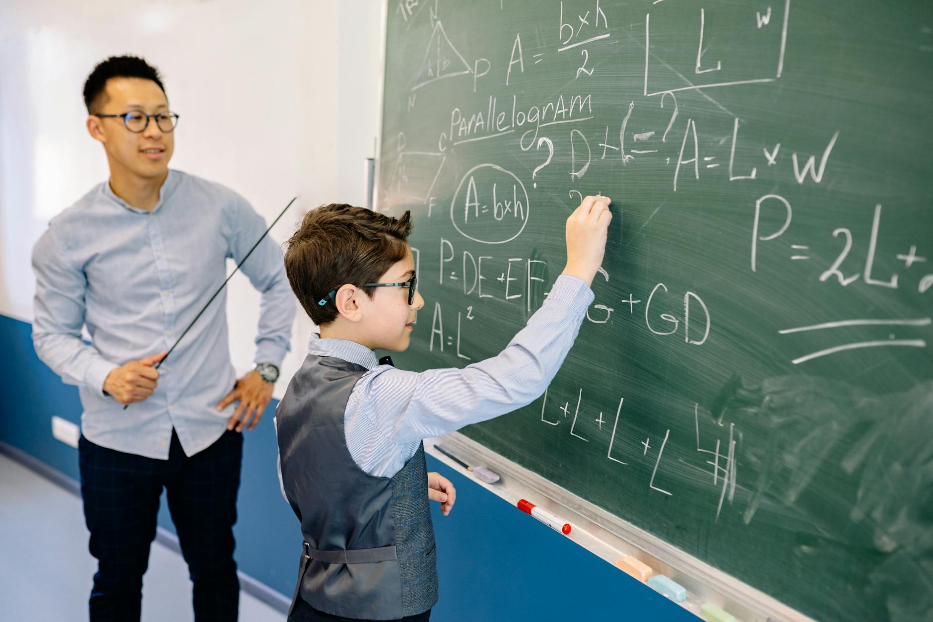 Nauczyciel pomaga uczniowi rozwiązywać zadania z matematyki na tablicy
