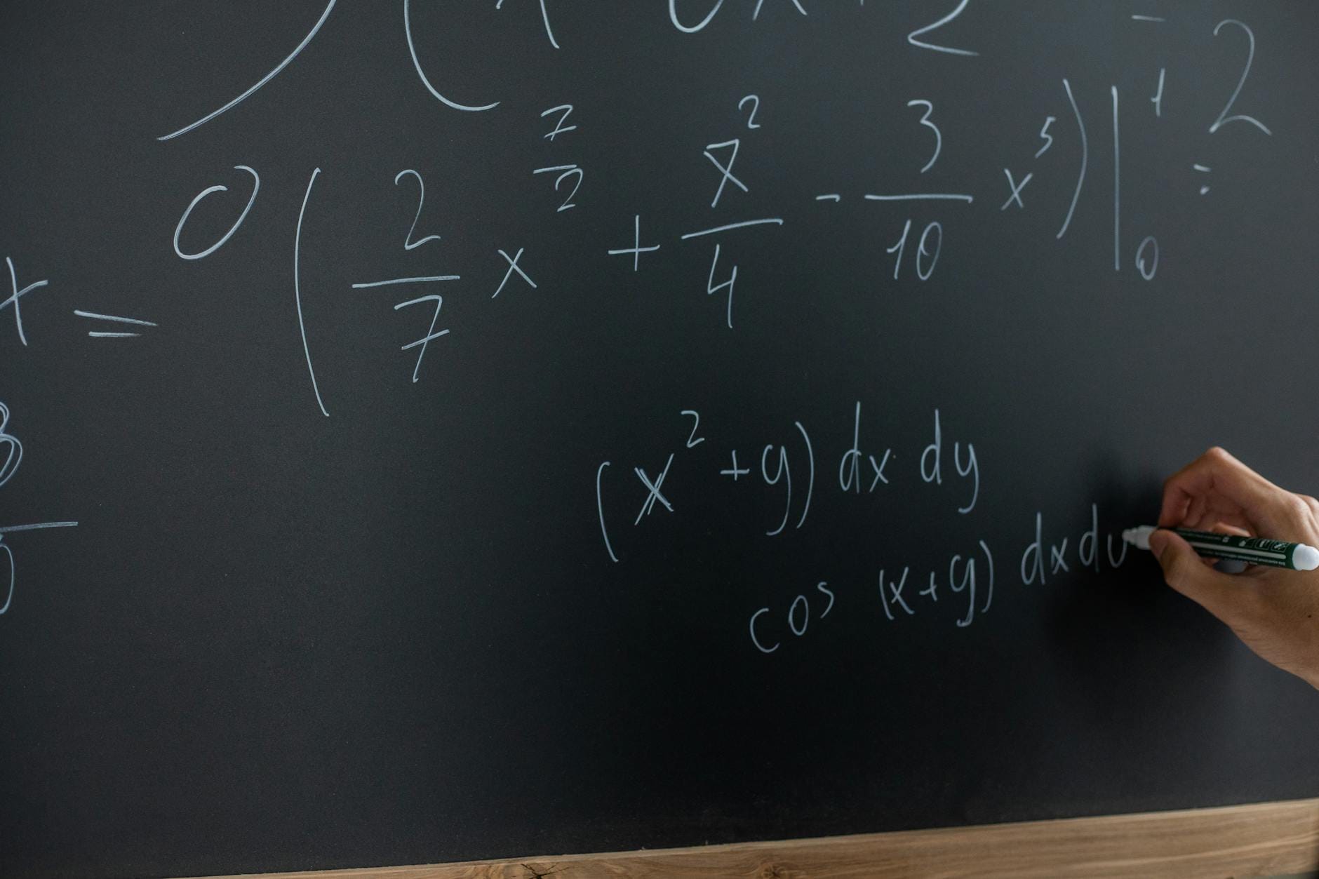 Ręka nauczyciela zapisuje równania matematyczne na tablicy w klasie