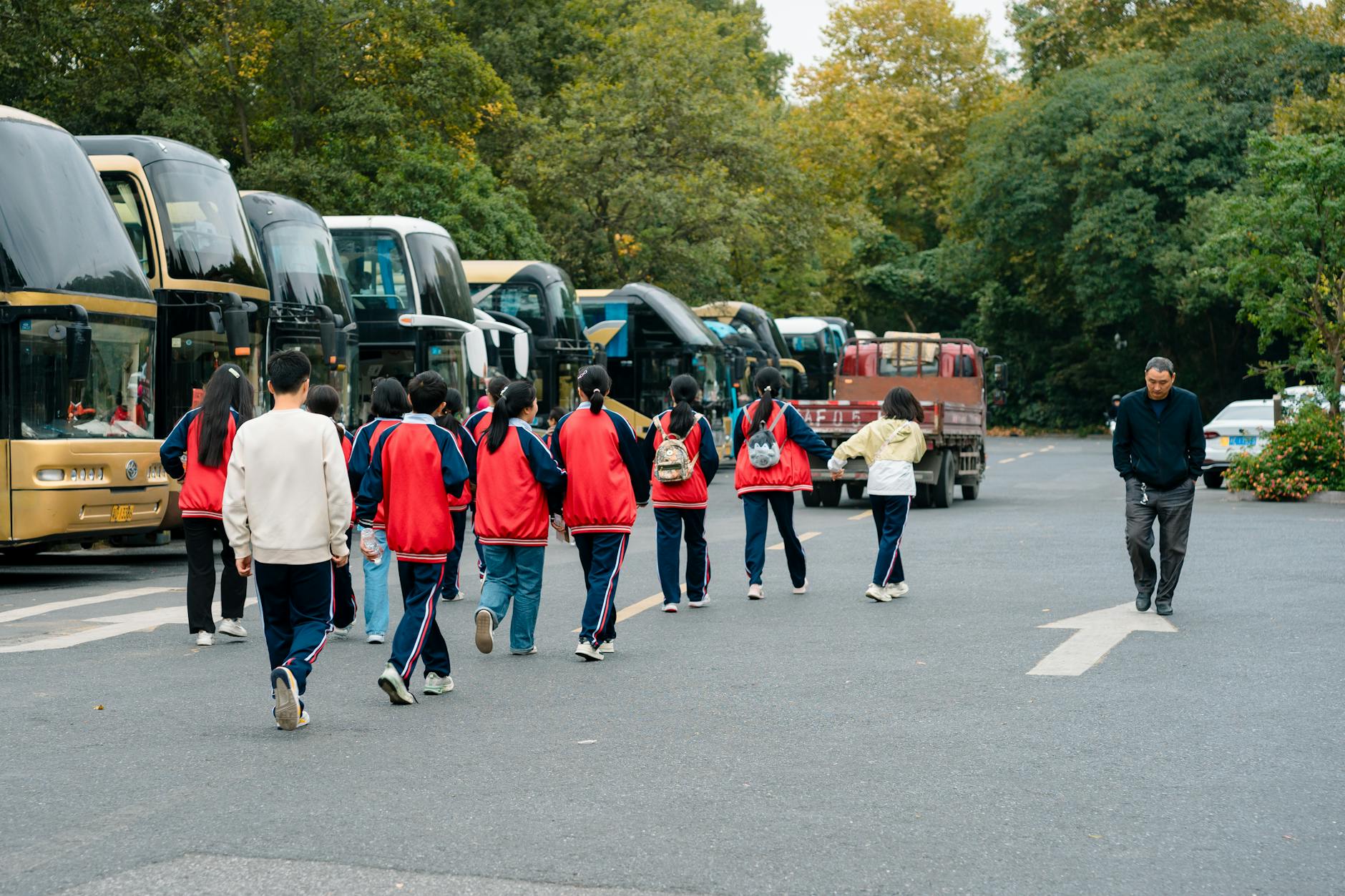 Uczniowie w strojach sportowych idą do autokarów na parkingu