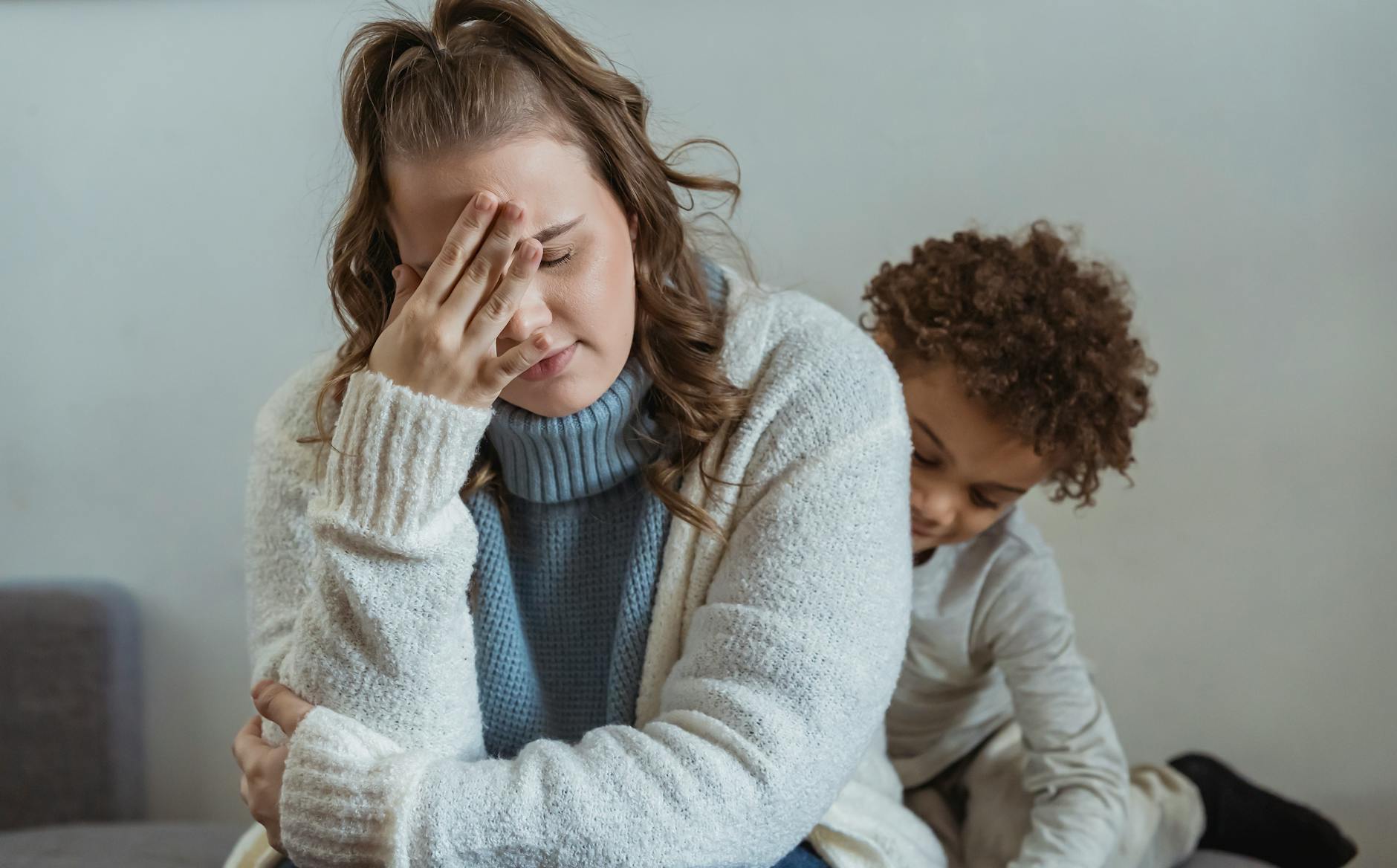 Zmęczona mama siedzi przy zamyślonym synu pod ścianą w domu