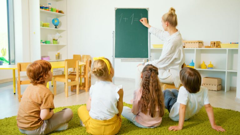 Nauczyciel prowadzi lekcję matematyki przy tablicy z młodszymi uczniami